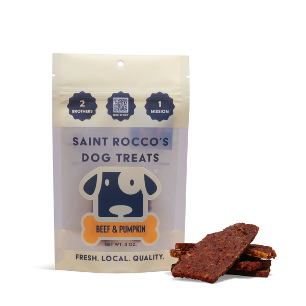 A bag of Beef and Pumpkin dog treats stands upright beside several rectangular pieces. The packaging shows a dog illustration with text emphasizing freshness, local ingredients, and quality in these all-natural dog treats.