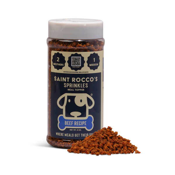 A plastic container labeled Beef Sprinkles - 8 pack displays a cartoon dog face, with a small mound of human-grade beef sprinkles in front of the container.