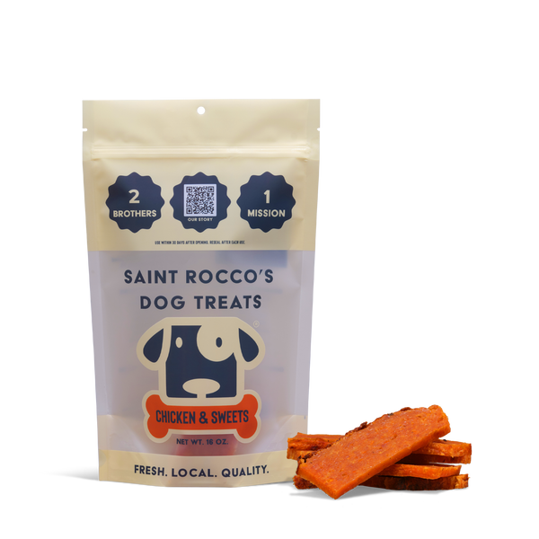 A bag of Chicken and Sweets training treats stands upright with orange treat sticks beside it. The packaging features a cartoon dog and emphasizes quality, local sourcing, and all-natural ingredients.