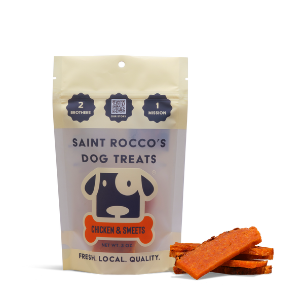 A bag of Chicken and Sweets Dog Treats stands upright beside several orange treat slices. The package features a dog graphic and highlights freshness, local quality, and that these are all-natural dog treats.