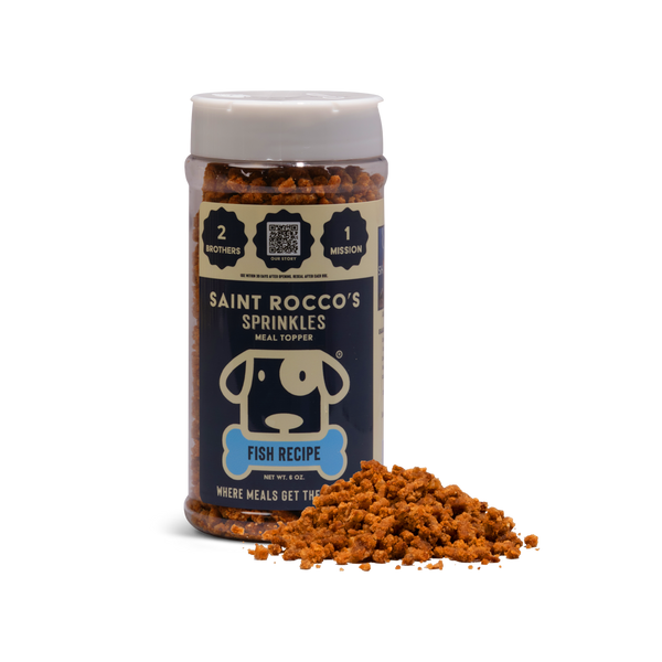 A clear plastic container labeled Fish Sprinkles - 8 pack stands upright, featuring wild-caught Alaskan salmon. Orange-brown fish sprinkles are spilled in front on a plain white background.